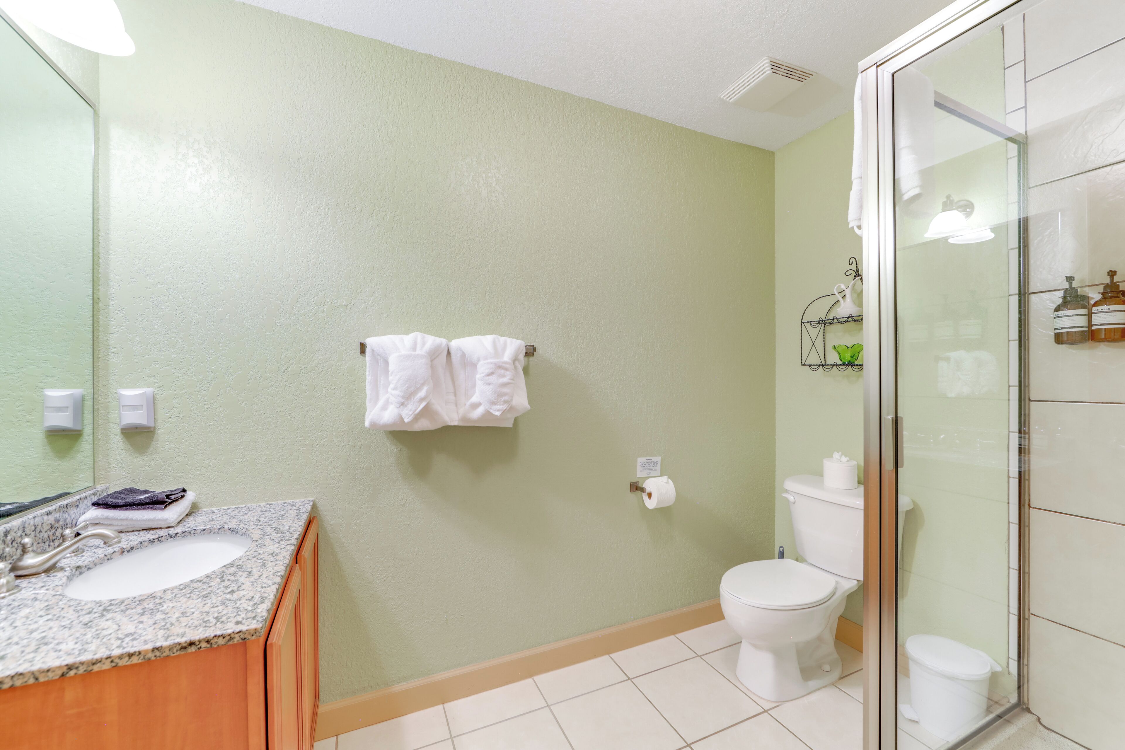 A bathroom with a granite sink, white toilet, and a glass shower enclosure.