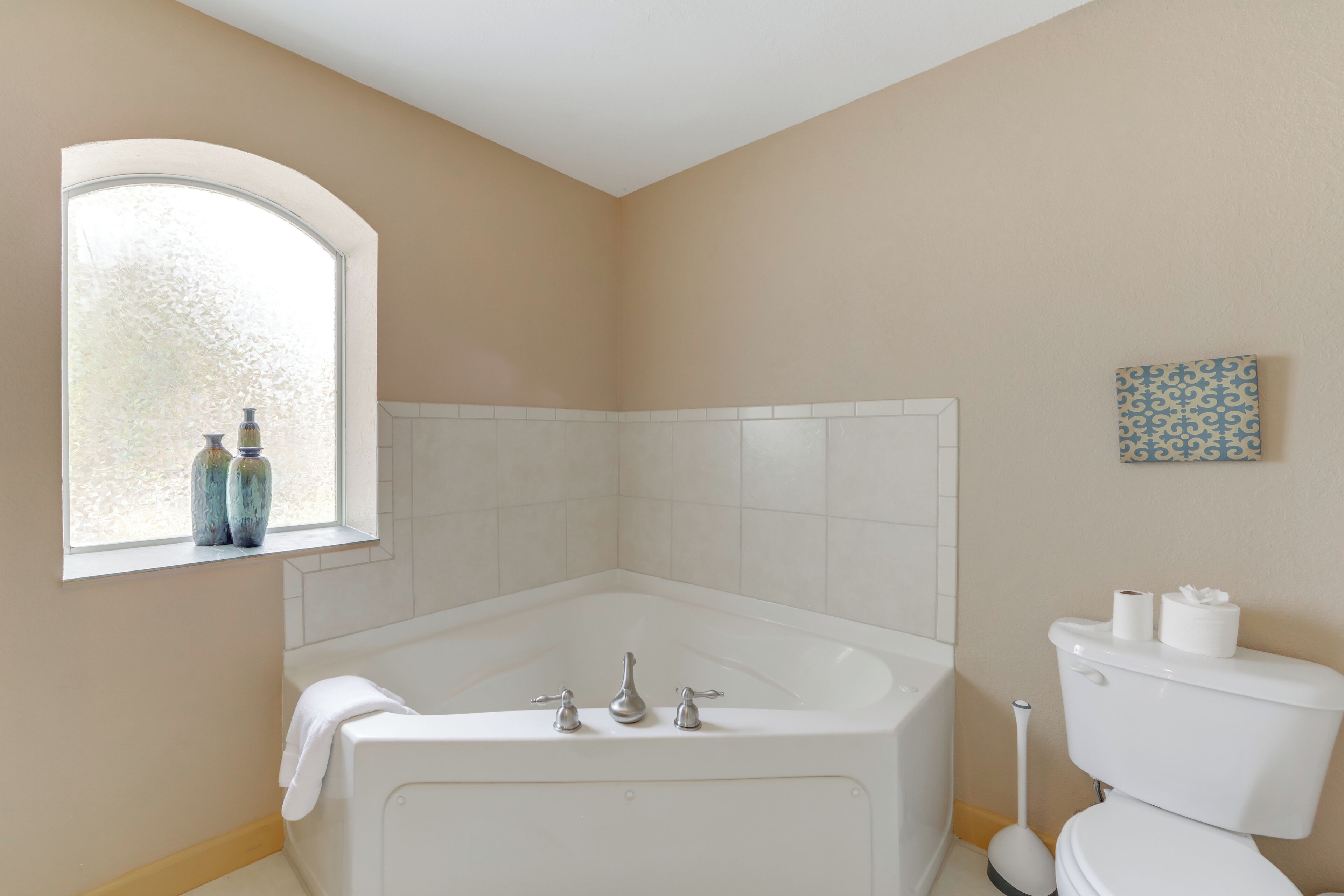 A bathroom with a bathtub, toilet, and a window with decorative bottles.