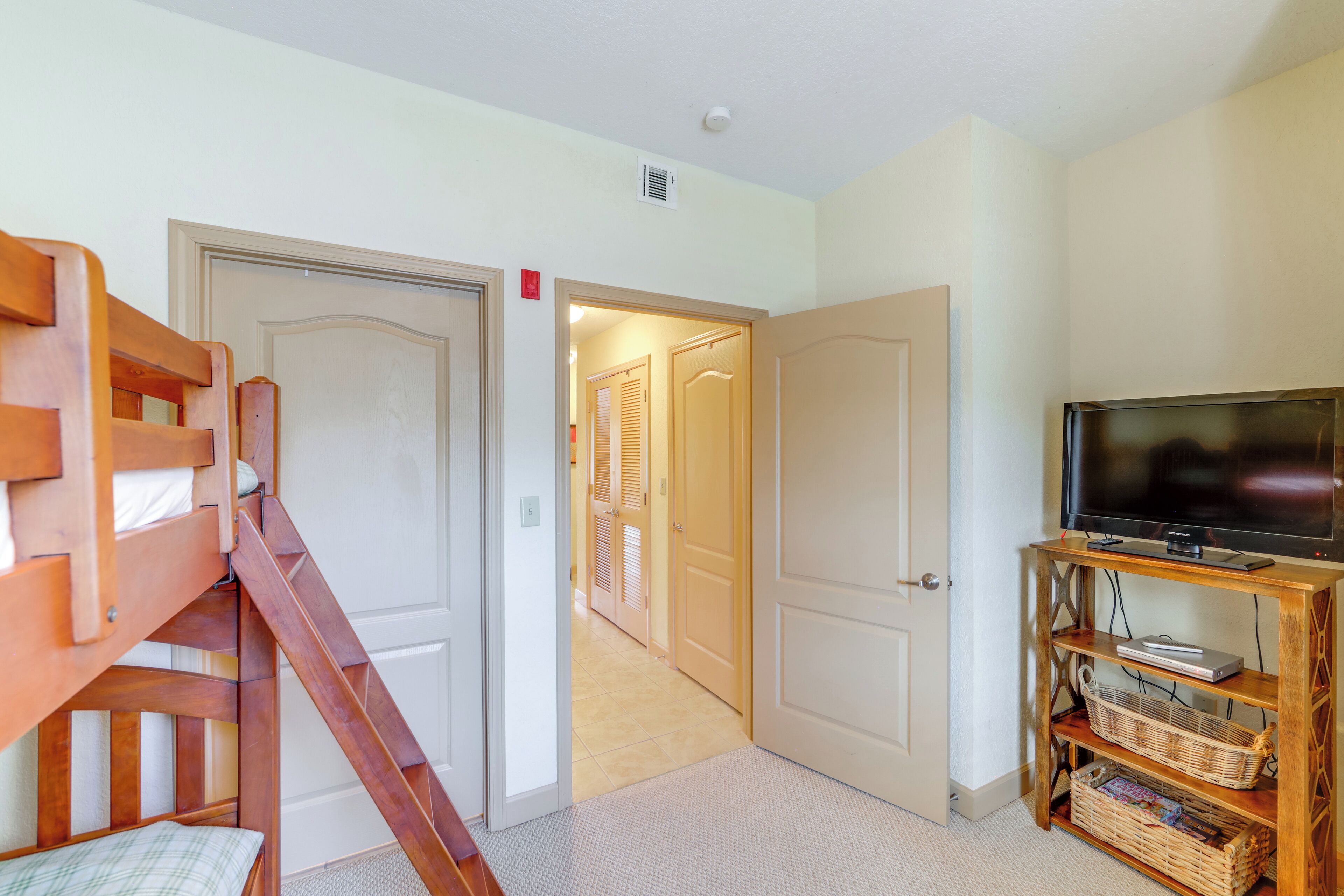 A room with a bunk bed, a television on a wooden stand, and a hallway leading to another room.