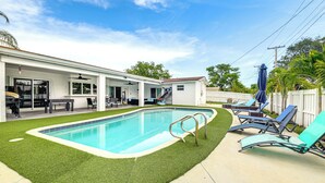 Ein Garten mit Swimmingpool, einer überdachten Terrasse und einem eingezäunten Bereich mit Liegestühlen.