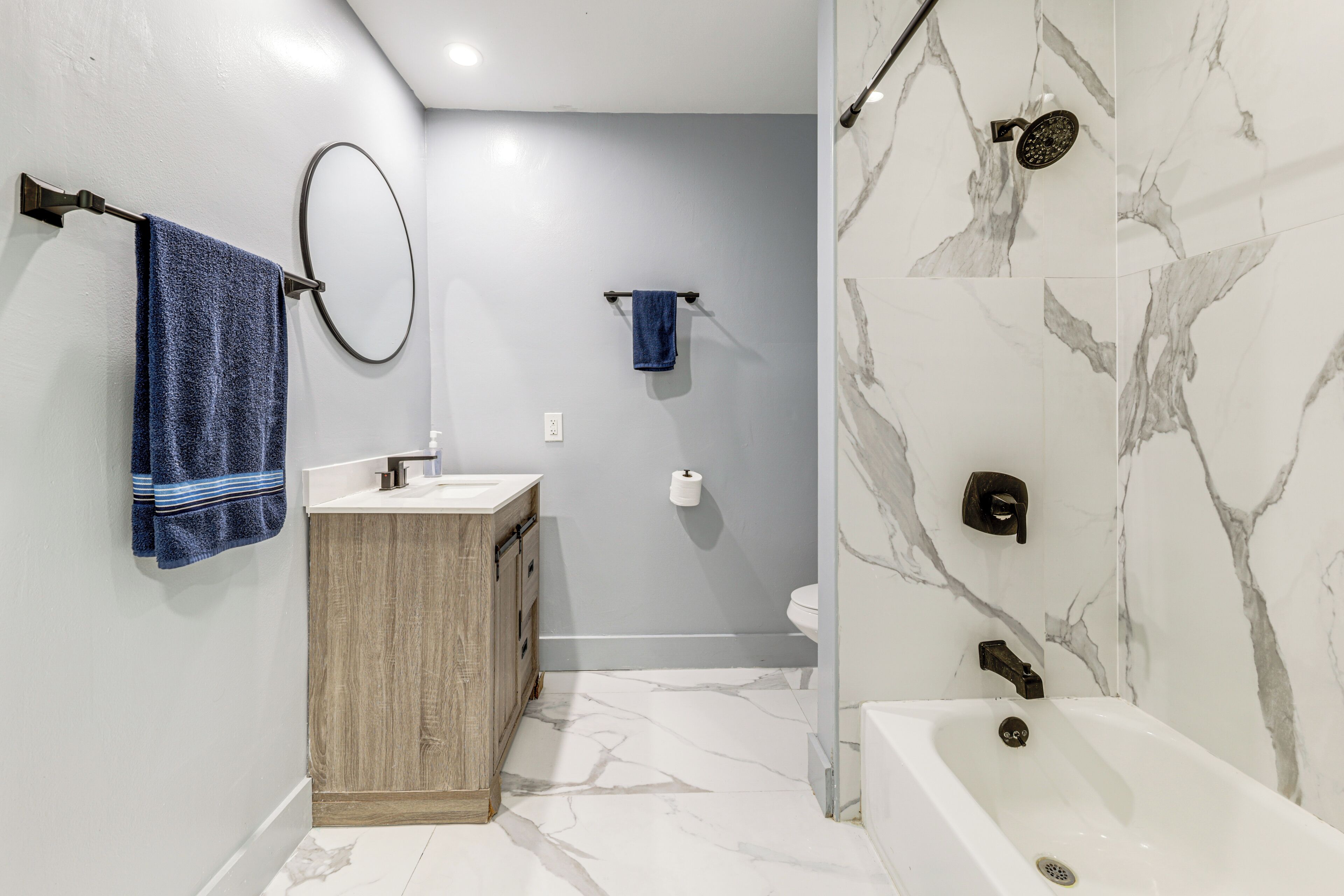 Un baño con piso de mármol, tocador de madera, lavamanos blanco, inodoro y bañera con ducha.