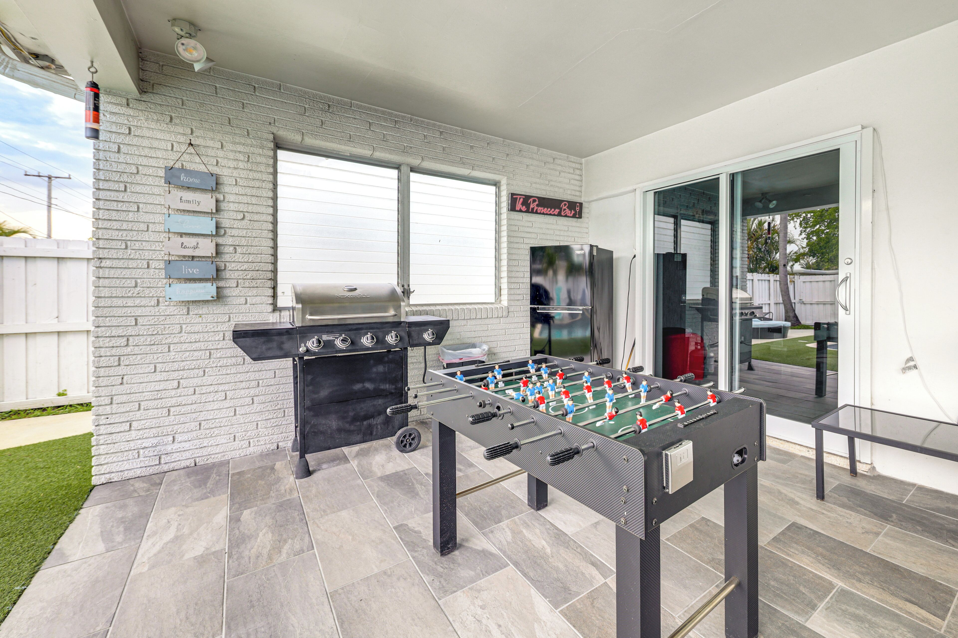 Un patio con mesa de fútbol de mesa, una parrilla y una puerta de vidrio que da a un jardín.