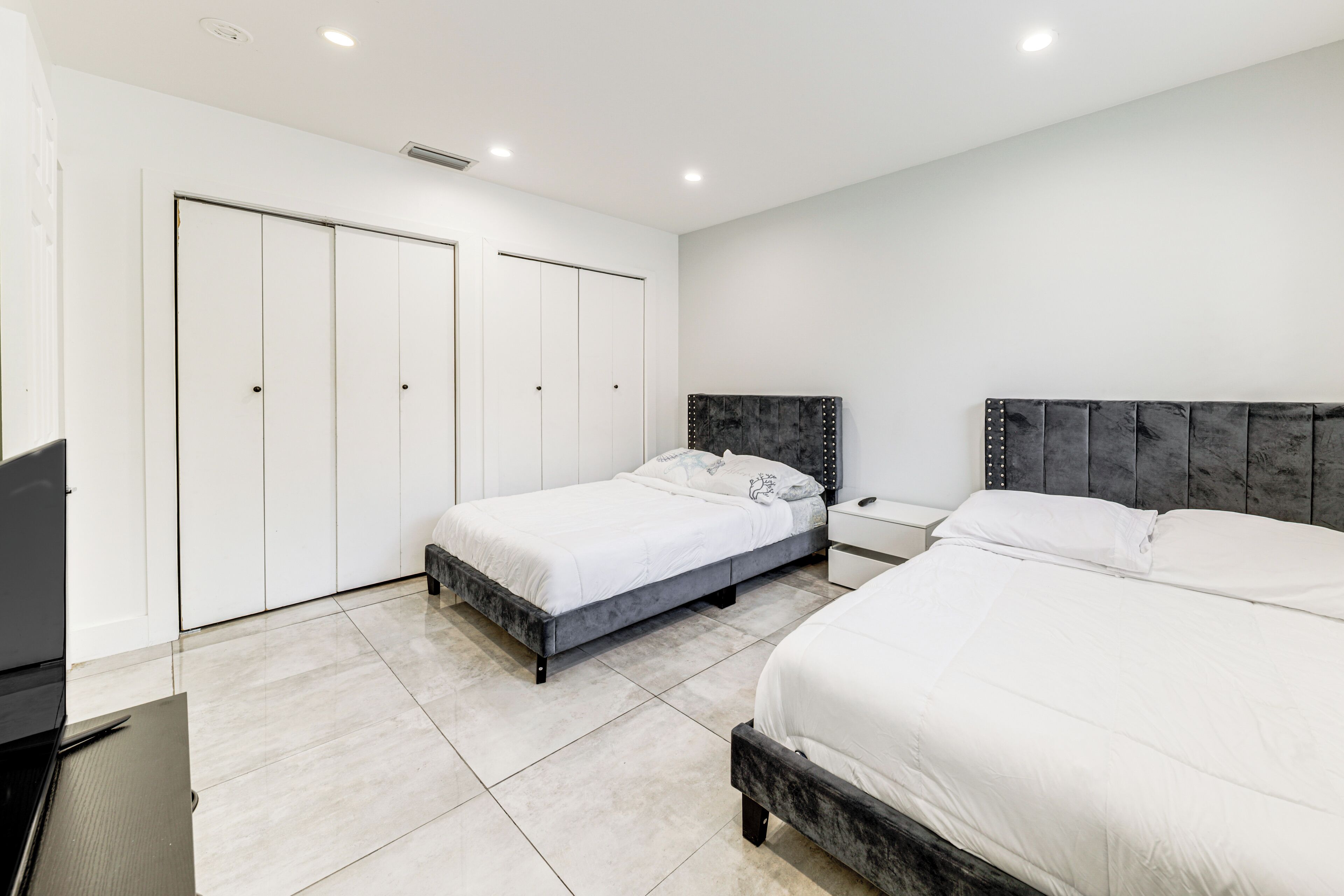 A modern bedroom with two beds, a desk, and a wardrobe.