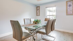 Un comedor con mesa de vidrio y sillas de cuero, obras de arte en las paredes y una ventana que proporciona luz natural.