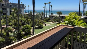 A balcony with a view of the ocean, surrounded by palm trees and a well-maintained garden. - Beautifully Updated One Bedroom with Beautiful Ocean views! (Oceanside)