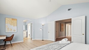 Un dormitorio moderno con una cama, un escritorio y una silla. Se ve un pasillo que da a otras habitaciones.
