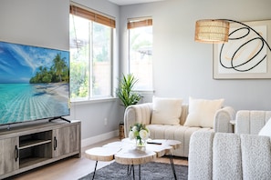 A modern living room with a large flat-screen TV, a grey sofa, a coffee table, and a floor lamp.