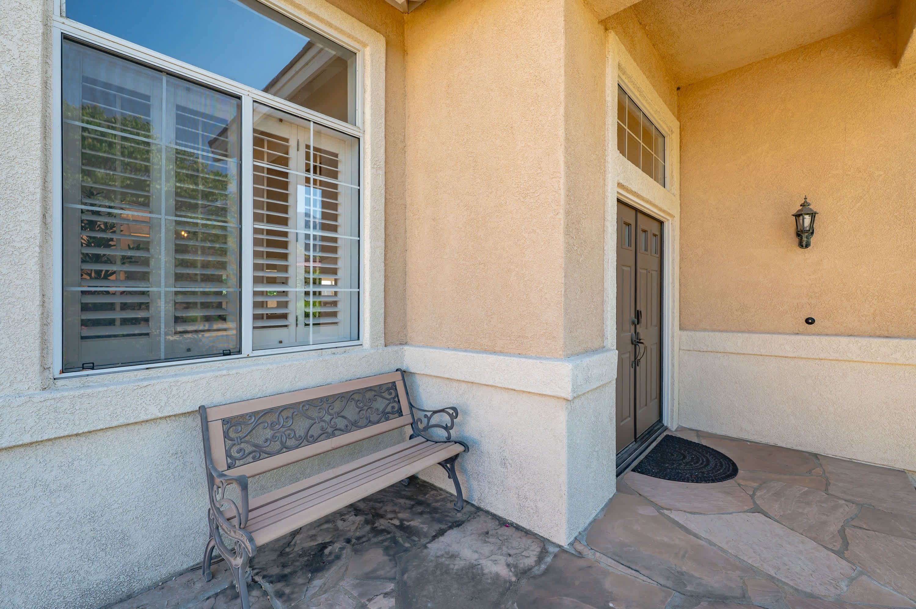 A stone-paved entrance with a bench, a door, and a window with blinds.