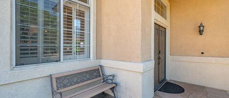 A stone-paved entrance with a bench, a door, and a window with blinds.