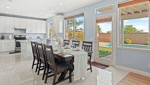 Una cocina moderna con armarios blancos, una isla central y una zona de comedor con una mesa dispuesta para cuatro.