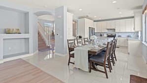 Una cocina moderna con armarios blancos, una zona de comedor con una mesa y sillas de madera, y una escalera que sube a otro nivel.