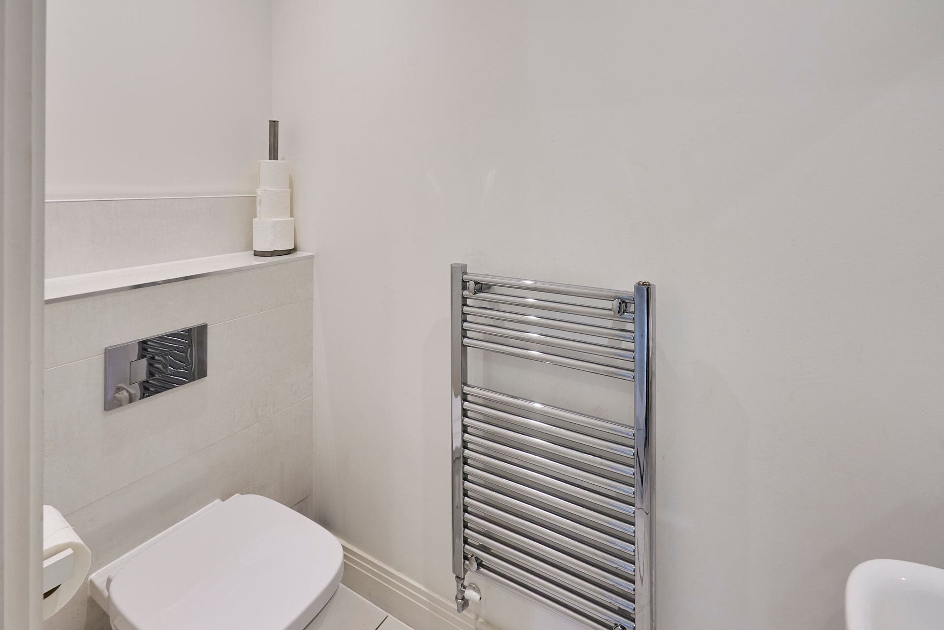 A small, modern bathroom with a white toilet, a metal towel rack, and a wall-mounted toilet paper holder.