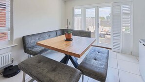 A dining area with a wooden table, grey upholstered benches, and a potted plant.