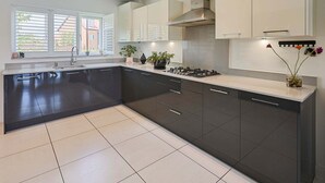 A modern kitchen with dark cabinets, a stainless steel range hood, and a large window with blinds.