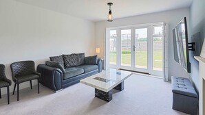 A modern living room with a glass-top coffee table, a grey sofa, and matching armchairs.