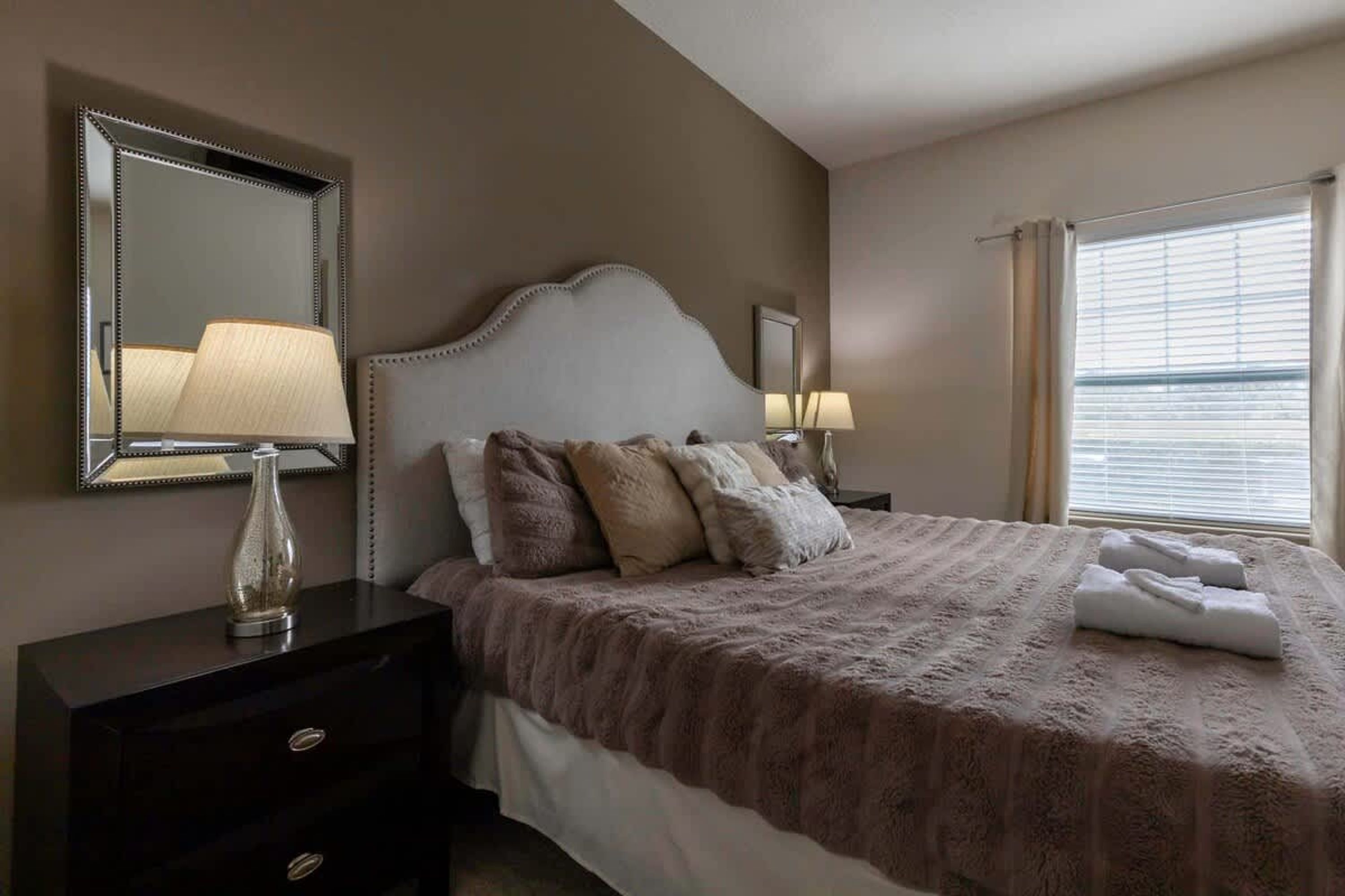 Habitación de hotel con una cama grande, una mesita de noche con lámpara, un aparador y una ventana con cortinas.