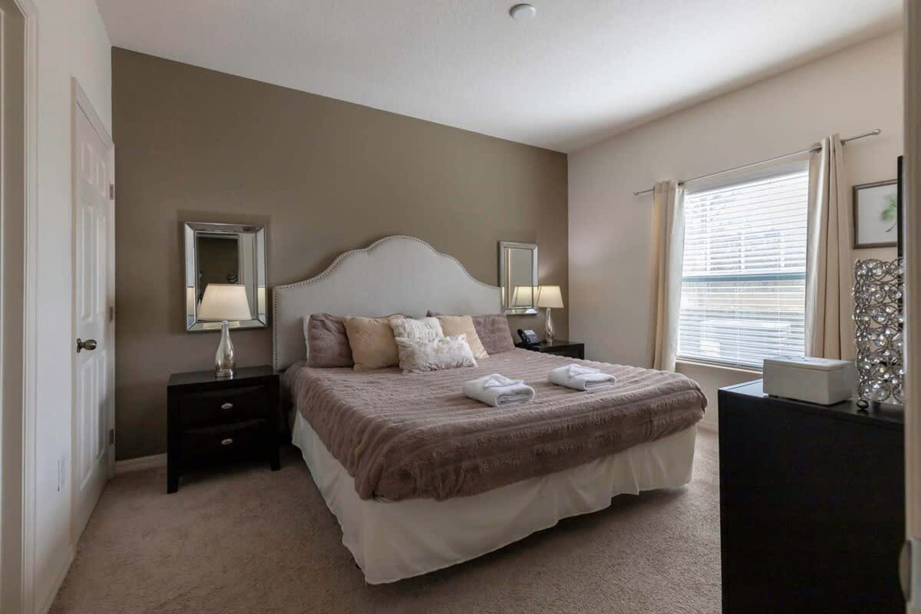 A bedroom with a large bed, two bedside tables, a dresser, and a window with blinds.