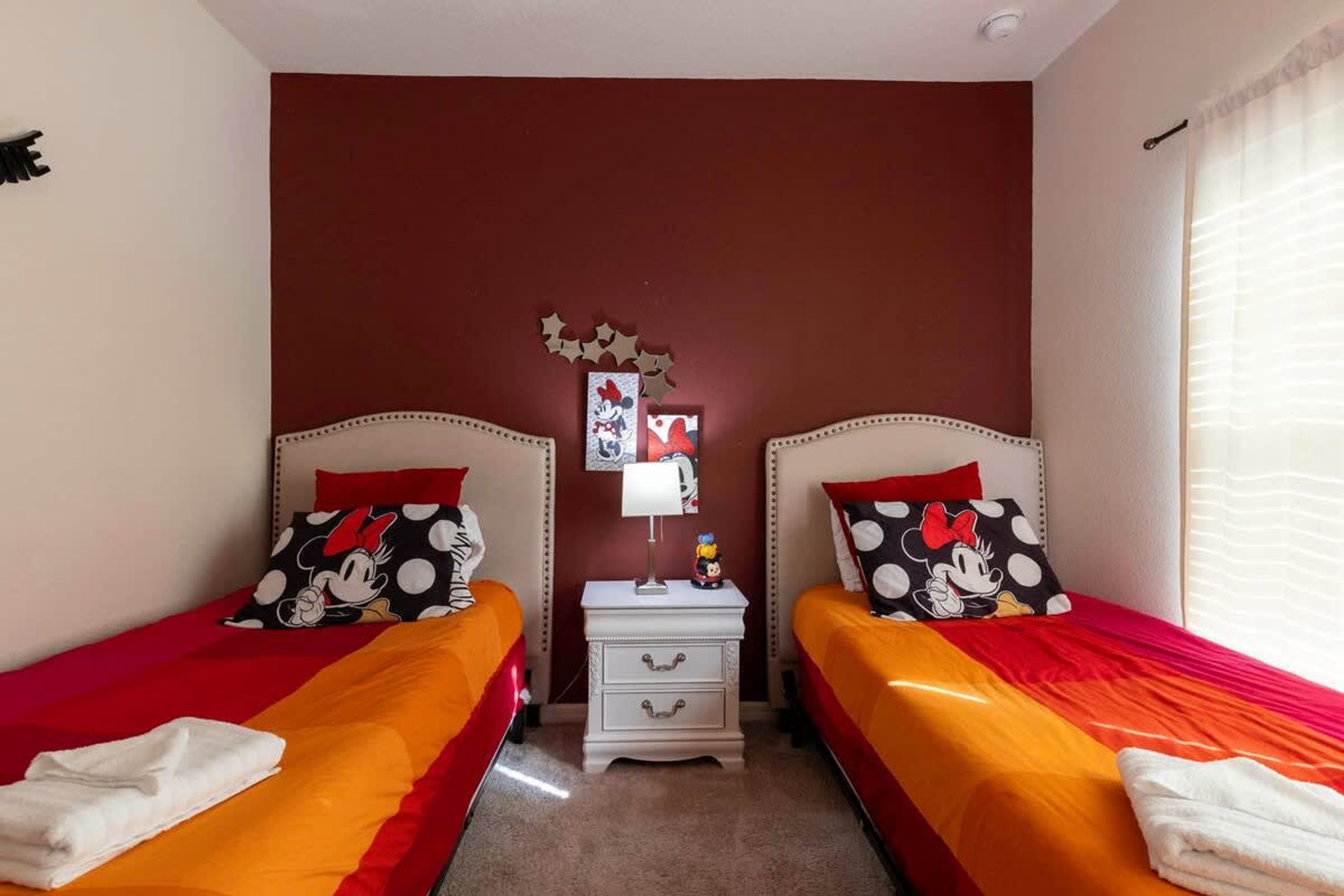A room with two beds, each with red and white bedding, and a small bedside table with a lamp and a Mickey Mouse figurine.
