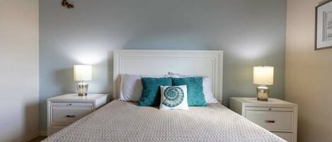 Een net opgemaakt bed met een beddegoed met patroon, twee nachtkastjes met lampen, en een muur met een klein decoratief object.