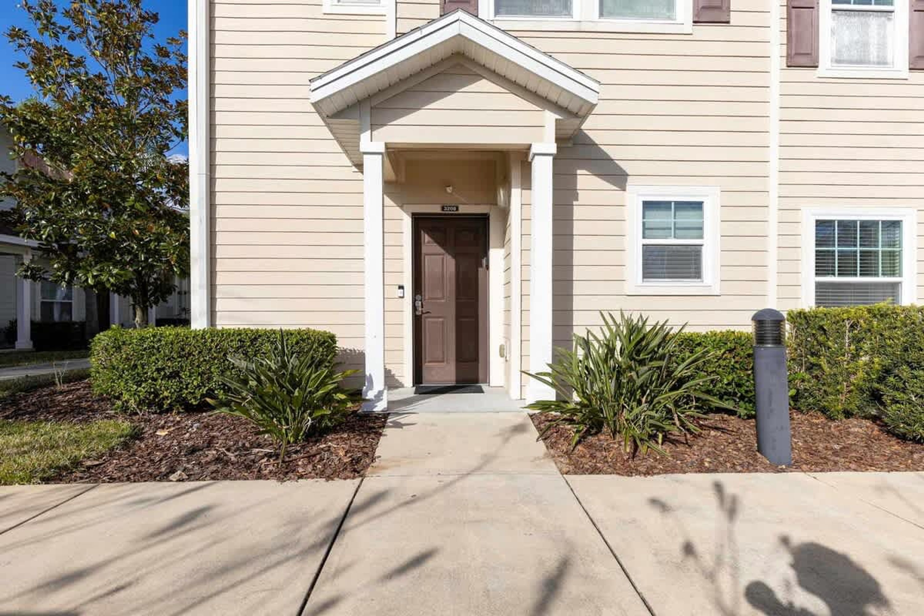 A beige building with a brown door, white columns, and a small porch.