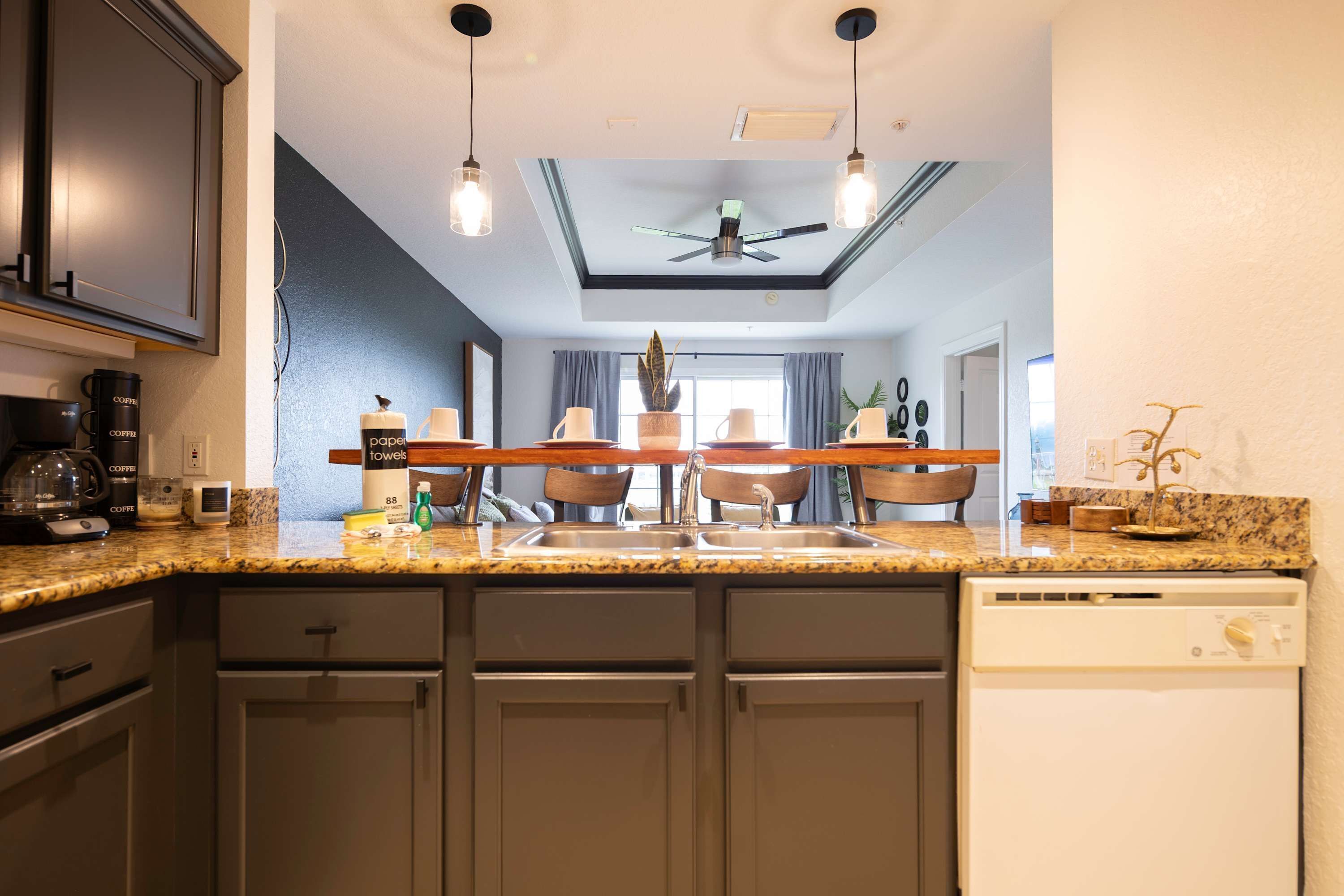 A modern kitchen with granite countertops, a built-in dishwasher, and a ceiling fan.