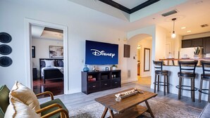 Una sala de estar moderna con un televisor de pantalla plana, una mesa de centro de madera y un comedor con taburetes de bar.