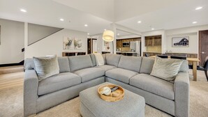 A modern living room with a sectional sofa, a wooden coffee table, and a dining area in the background.