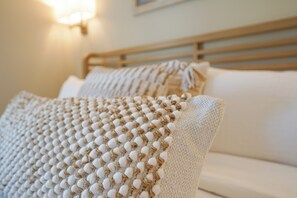 A bed with a textured blanket and pillows, a wooden headboard, and a wall-mounted light fixture. - Big Rock Retreat - Waterfont Getaway in the Heart of Morehead City! (Morehead City)