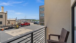 A balcony with a view of a parking lot, a building with multiple windows, and a chair.
