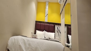 Une chambre d’hôtel avec un lit, un miroir et un mur d’accent jaune.