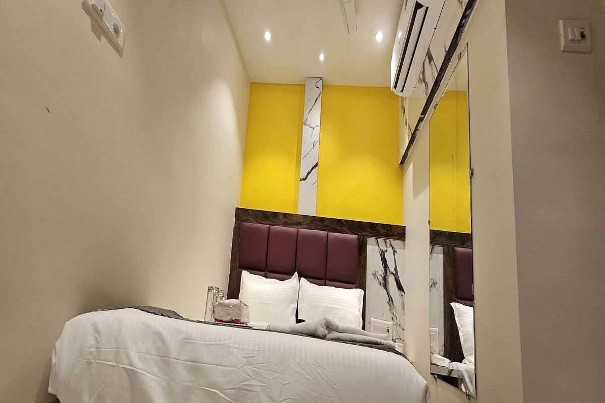 Una habitación de hotel con cama, espejo y pared de acento amarilla.