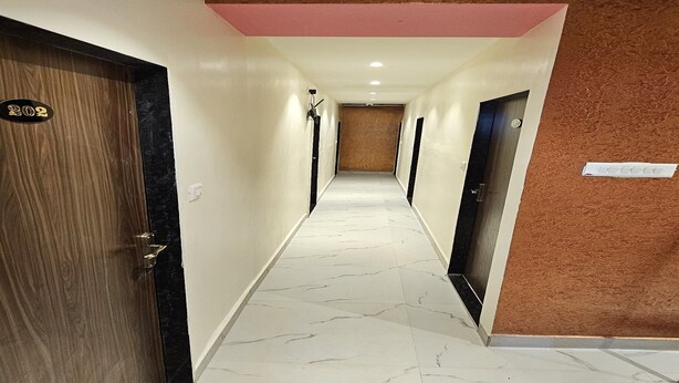 Un couloir d’hôtel avec un sol en marbre, des portes en bois et un plafond rose.