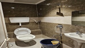 Une salle de bain moderne équipée de toilettes, d’un bidet, d’un lavabo et d’un seau bleu avec un gobelet jaune.