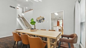 A dining area with a wooden table and brown chairs, a staircase, and a wall-mounted decorative plate arrangement. - Best of Garland | Pool, Cinema Rm, BBQ (3BD/2.5BA) (Garland)