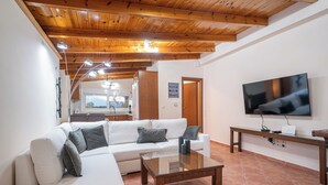 A living room with a wooden ceiling, white sofa, and a flat-screen TV mounted on the wall. -  Ζερβάτα Σάμης 6 ατομων 5 λ από τη Σάμη
Ιδανικό για χαλάρωση   (Grizata)
