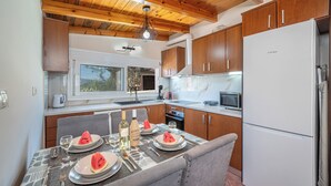A modern kitchen with wooden cabinets, a white refrigerator, and a dining table set for two with plates of watermelon and wine glasses. -  Ζερβάτα Σάμης 6 ατομων 5 λ από τη Σάμη
Ιδανικό για χαλάρωση   (Grizata)