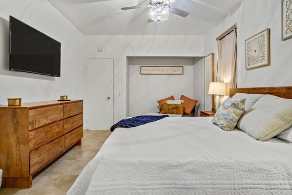 Un dormitorio con cama, cómoda de madera, televisor, ventilador de techo y decoración mural.