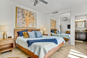 Ein Schlafzimmer mit einem großen Bett, Nachttischen, einem Spiegel und Kunstwerken an den Wänden.
