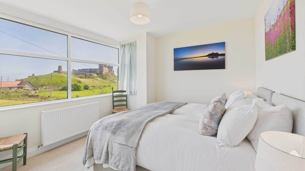 A bedroom with a large window, a bed, a chair, and a radiator. - Host & Stay | Chirnells (Bamburgh)