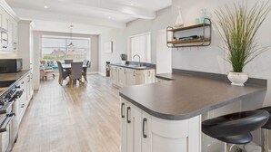 A modern kitchen with a central island, a dining area with a view, and a bar area with a plant. - Host & Stay | Chirnells (Bamburgh)