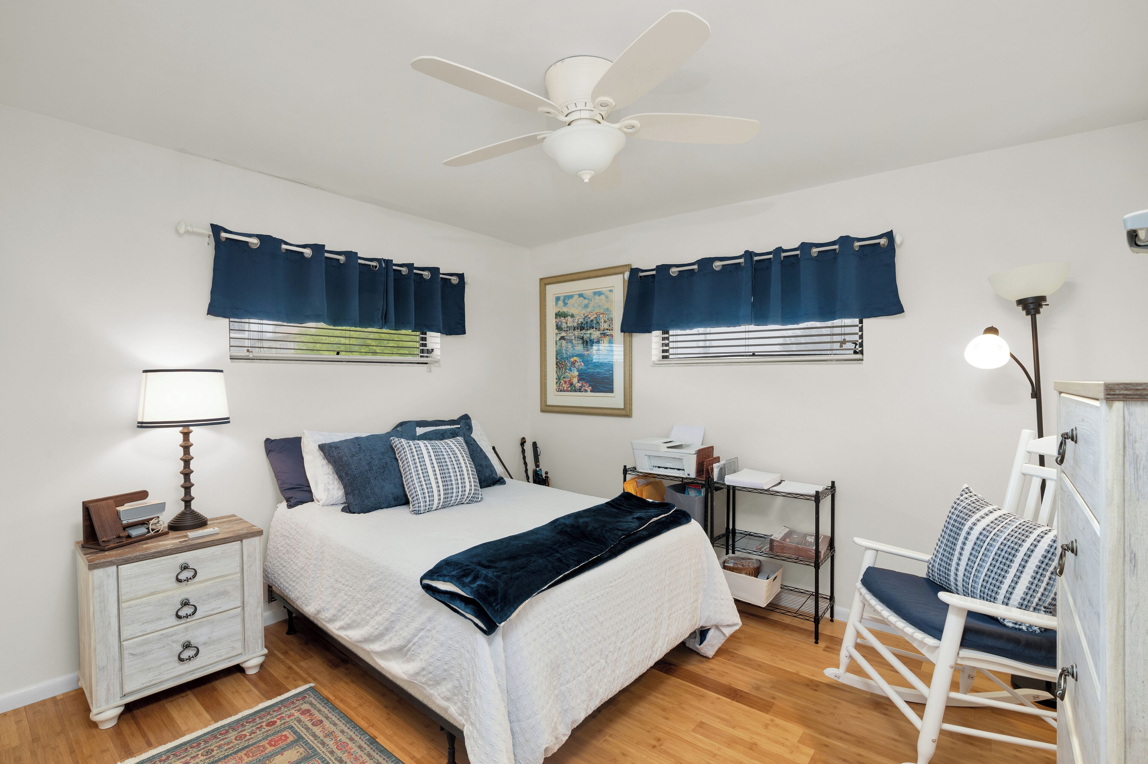 Une chambre à coucher comprenant un lit, une table de chevet, une commode, une chaise et un ventilateur de plafond.