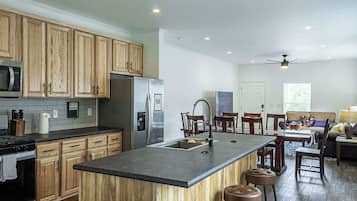 Una cocina moderna con armarios de madera, electrodomésticos de acero inoxidable, una isla central con taburetes y un comedor con ventilador de techo.