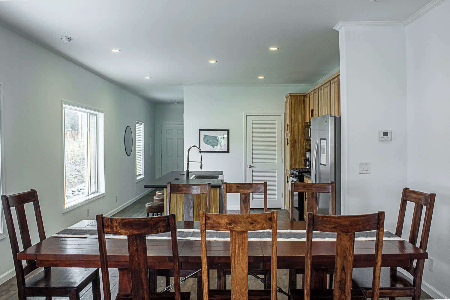 A dining area with a wooden table and chairs, a kitchen with wooden cabinets, and a view of the backyard through a window.