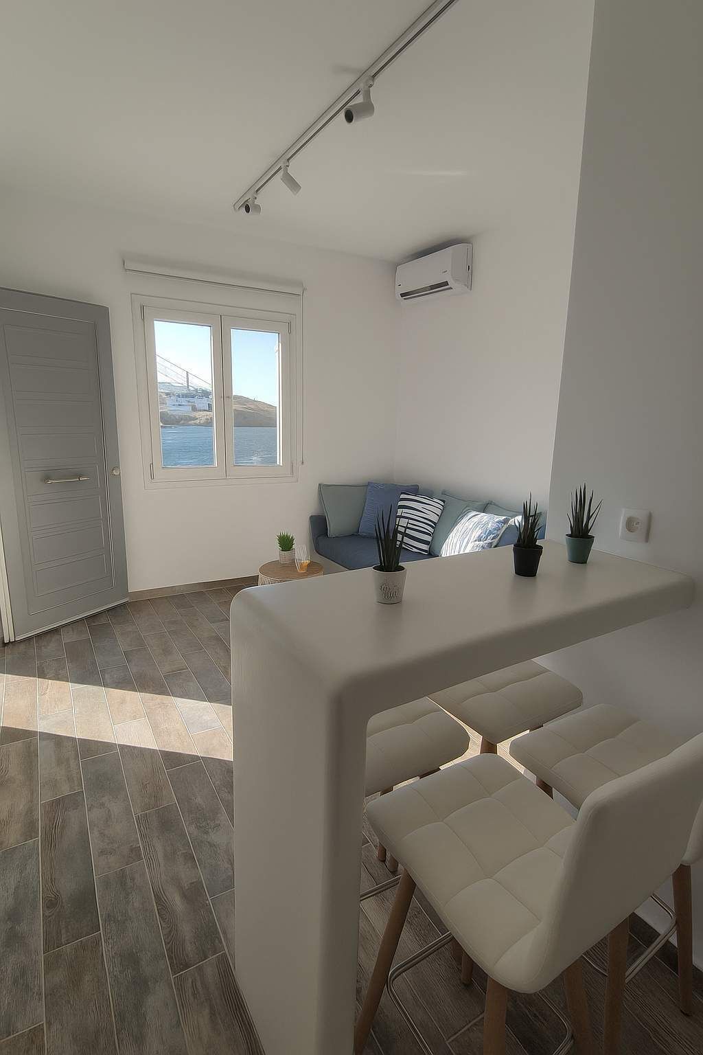 Un saló modern amb un sofà, una zona de menjador amb taula i cadires, i una finestra gran que dona a mar.