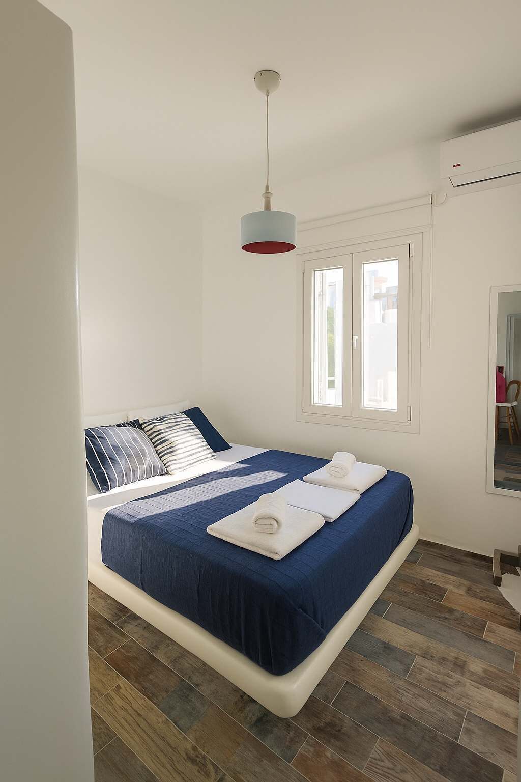 Ein Schlafzimmer mit Bett, einer Hängelampe, einem Fenster und einem Spiegel.