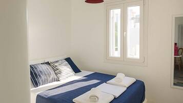 Ein Schlafzimmer mit Bett, einer Hängelampe, einem Fenster und einem Spiegel.