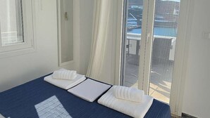 A modern bedroom with a large bed, a ceiling light, and a view of the outdoors. - Seafront Alos Gem - Loutra Seaview Escape (Loutra)