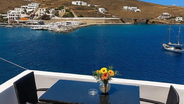 A terrace with a table and chairs overlooking a coastal town, a clear blue sky, and a body of water with boats. - Seafront Alos Gem - Loutra Seaview Escape (Loutra)