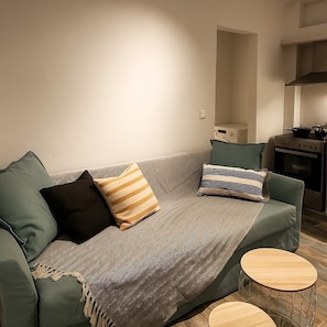 Una sala de estar con un sofá, dos mesas auxiliares y una cocina con estufa.