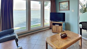 A living room with a large window, a television, and a wooden coffee table. - Watercolor Skies | Cozy, Waterfront (Corpus Christi)